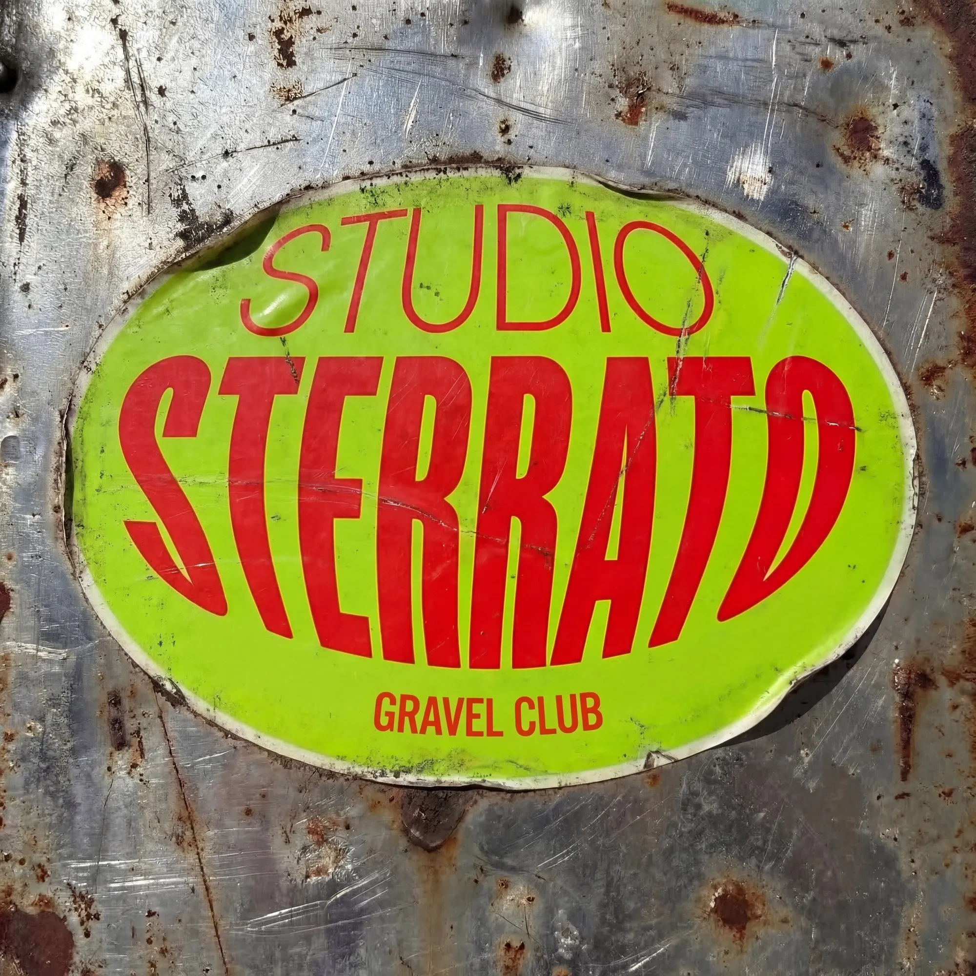 Lo sticker ovale Studio Sterrato Gravel Club incollato su una lastra di metallo graffiata e arrugginita